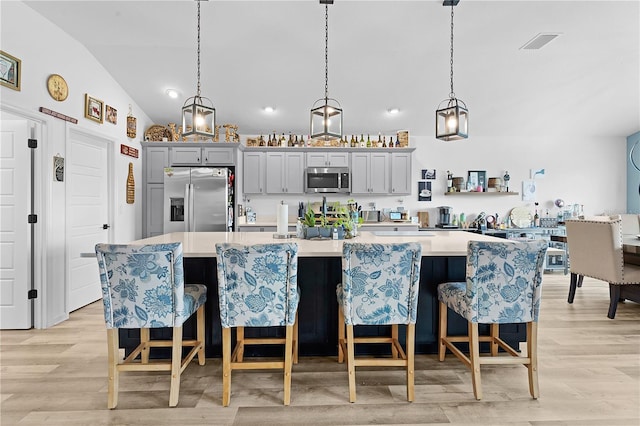 kitchen featuring lofted ceiling, a kitchen bar, stainless steel appliances, hanging light fixtures, and gray cabinets