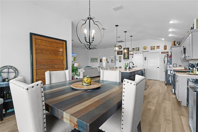 dining room featuring vaulted ceiling, sink, a chandelier, and light hardwood / wood-style flooring