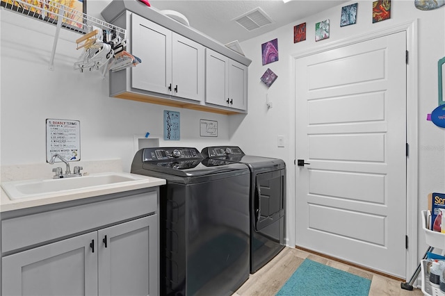 laundry area featuring washer and dryer, sink, light hardwood / wood-style flooring, and cabinets