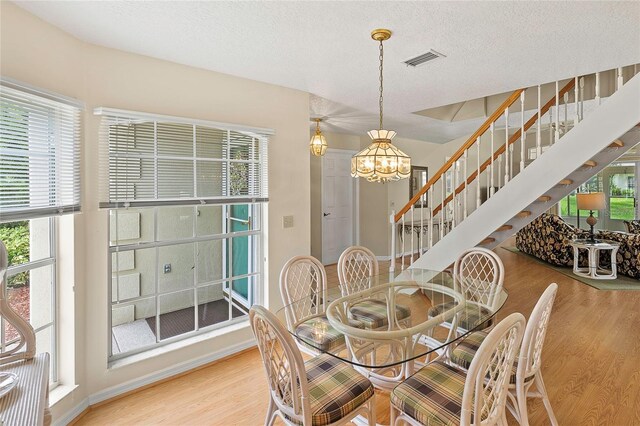 dining area with light wood-type flooring, an inviting chandelier, and a textured ceiling