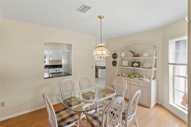 dining space featuring light wood-type flooring, a textured ceiling, and plenty of natural light