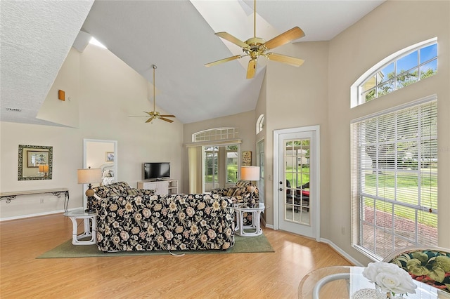 living room featuring baseboards, high vaulted ceiling, wood finished floors, and a ceiling fan