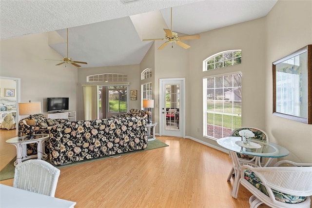 living room with wood finished floors, a ceiling fan, baseboards, and high vaulted ceiling