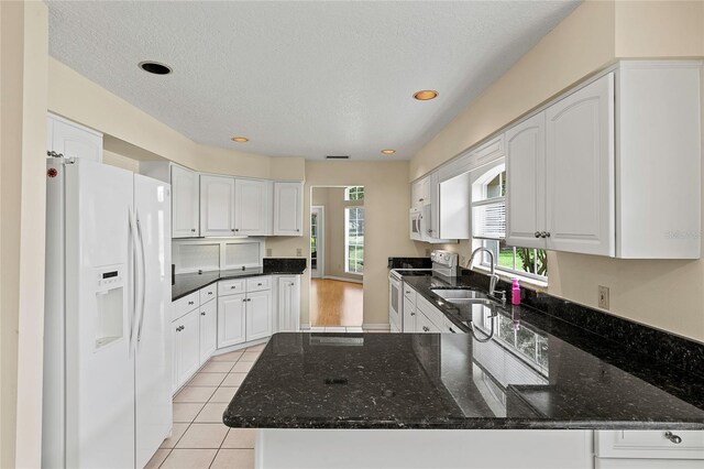 kitchen featuring dark stone countertops, white appliances, sink, and white cabinets