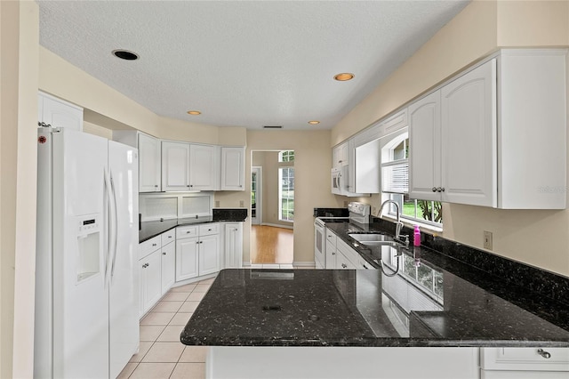 kitchen with a sink, dark stone counters, white appliances, and a peninsula