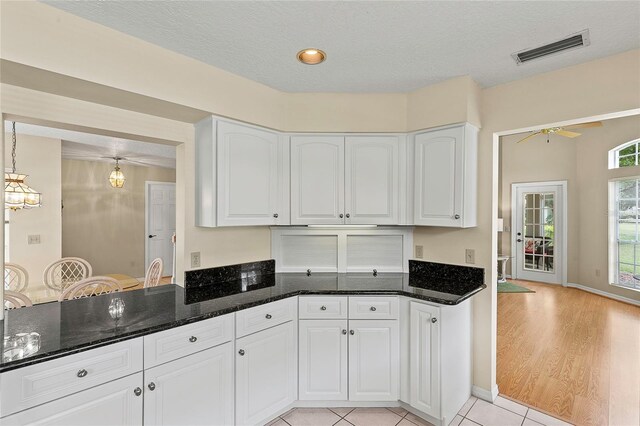 kitchen with light wood-type flooring, dark stone counters, a textured ceiling, and white cabinets