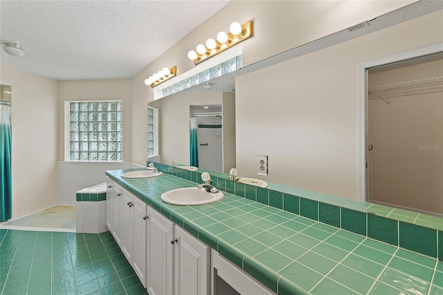 full bath with a sink, a textured ceiling, double vanity, and a walk in shower