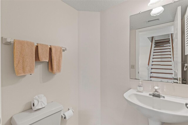 bathroom with a textured ceiling, toilet, and sink