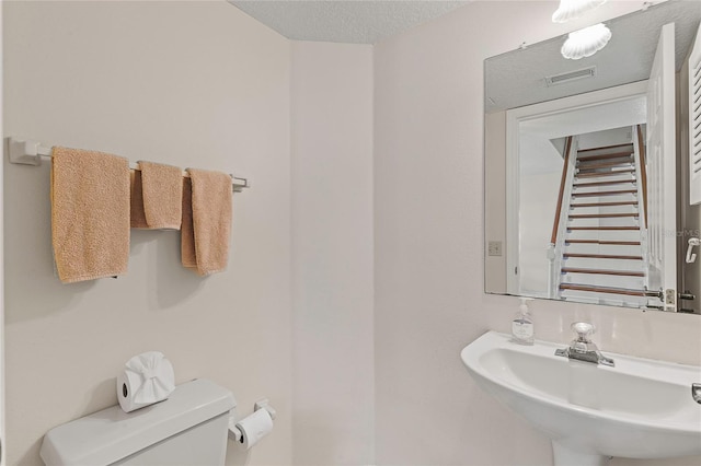 bathroom featuring a textured ceiling, toilet, visible vents, and a sink