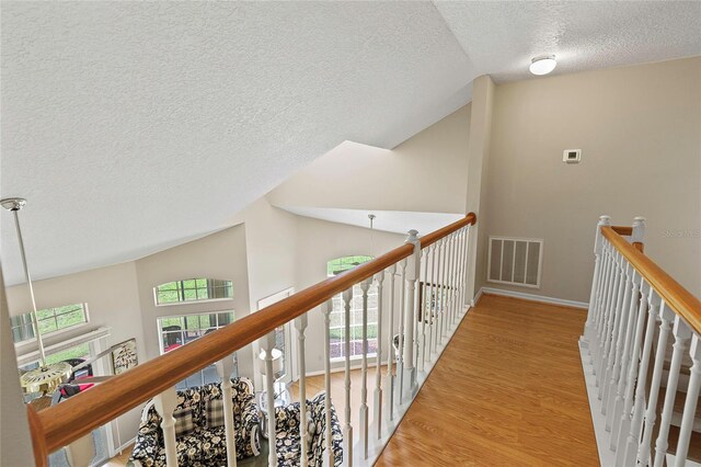 hall featuring lofted ceiling, plenty of natural light, light hardwood / wood-style floors, and a textured ceiling