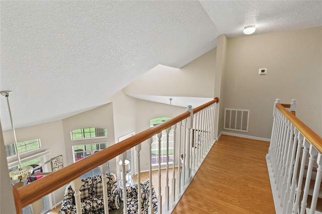 hallway featuring visible vents, baseboards, lofted ceiling, an upstairs landing, and wood finished floors