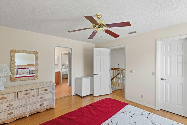 bedroom with ceiling fan, connected bathroom, a textured ceiling, and light hardwood / wood-style flooring