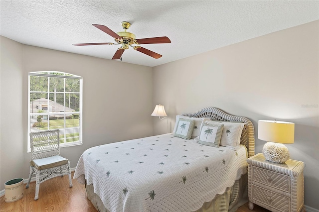 bedroom with baseboards, a textured ceiling, wood finished floors, and a ceiling fan