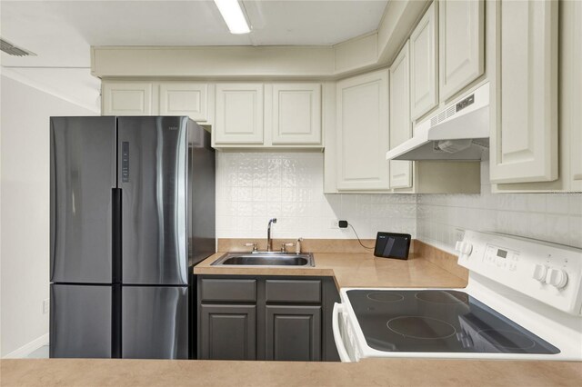 kitchen featuring cream cabinets, electric range, stainless steel refrigerator, sink, and decorative backsplash