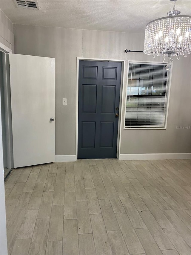 entryway featuring a textured ceiling, light hardwood / wood-style flooring, and a notable chandelier