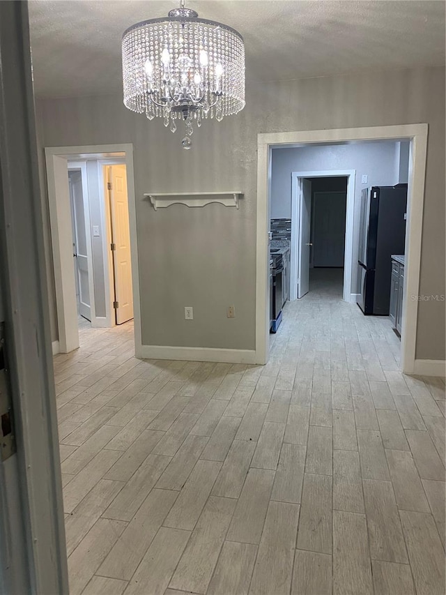 unfurnished dining area with a textured ceiling, an inviting chandelier, and light wood-type flooring