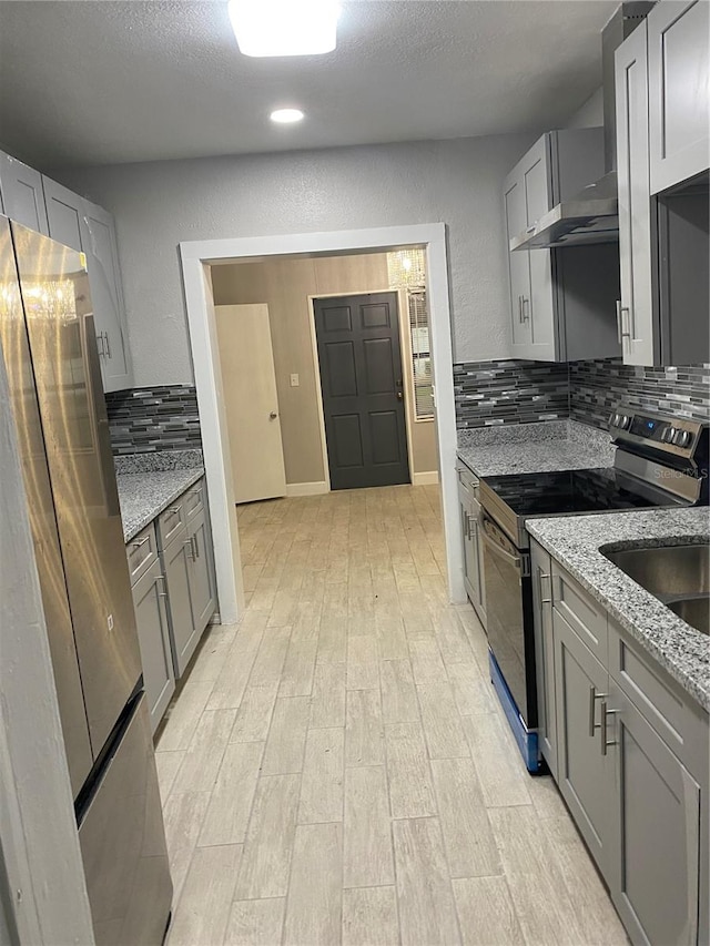 kitchen with a textured ceiling, light hardwood / wood-style flooring, light stone countertops, decorative backsplash, and appliances with stainless steel finishes