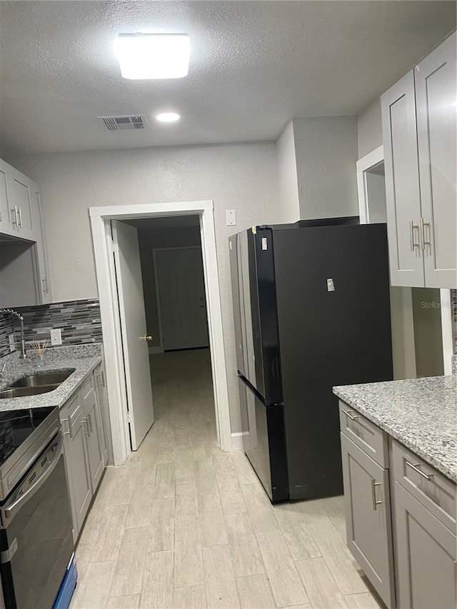 kitchen with stainless steel electric range, sink, black fridge, decorative backsplash, and a textured ceiling