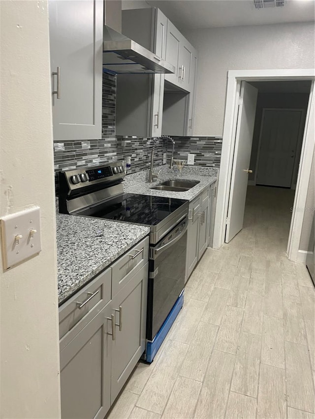 kitchen featuring wall chimney exhaust hood, tasteful backsplash, sink, light wood-type flooring, and stainless steel range with electric cooktop