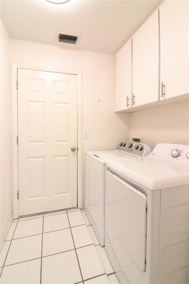 laundry area with light tile patterned flooring, washer and dryer, a textured ceiling, and cabinets