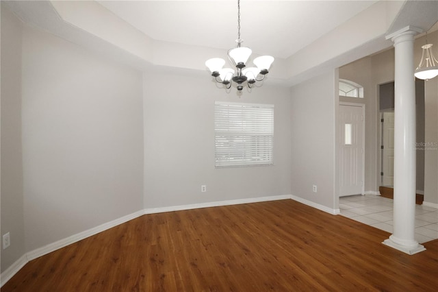 unfurnished room with ornate columns, a notable chandelier, light wood-type flooring, and a raised ceiling