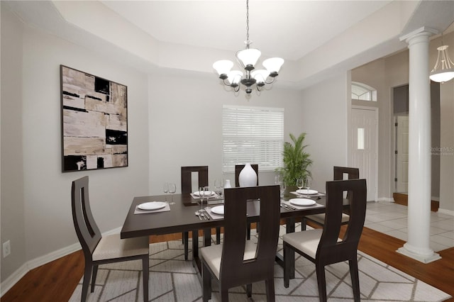 dining space featuring an inviting chandelier, ornate columns, light hardwood / wood-style floors, and a raised ceiling