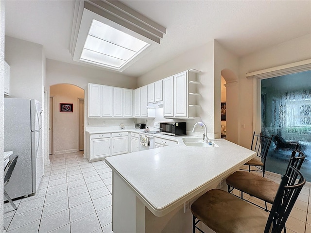 kitchen with white cabinetry, white appliances, sink, a breakfast bar, and kitchen peninsula