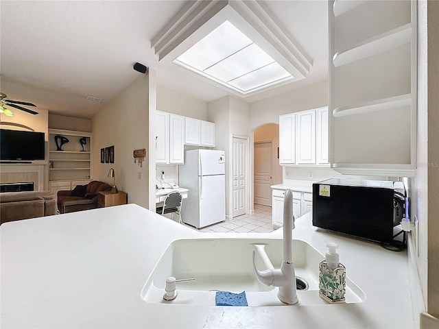 kitchen with a fireplace, white cabinetry, white refrigerator, light tile patterned floors, and ceiling fan