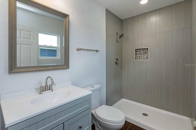 bathroom featuring vanity, toilet, tiled shower, and a textured ceiling