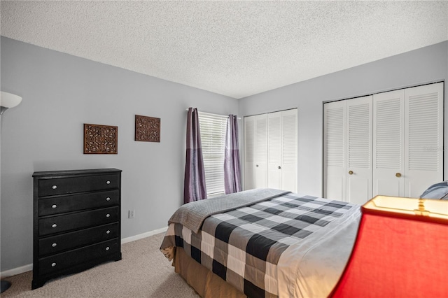 bedroom featuring multiple closets, a textured ceiling, and light colored carpet