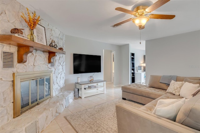 tiled living room with ceiling fan and a stone fireplace