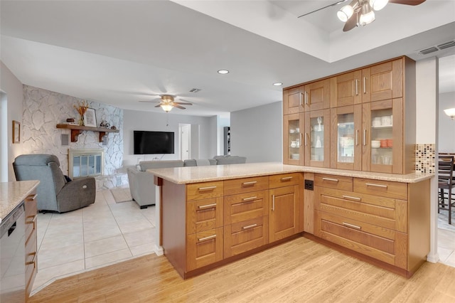 kitchen featuring light wood-type flooring, kitchen peninsula, ceiling fan, and a stone fireplace