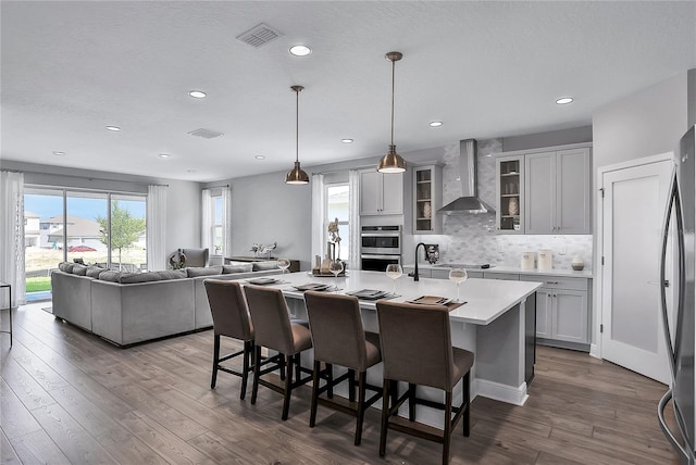 kitchen featuring wall chimney range hood, a kitchen breakfast bar, dark hardwood / wood-style floors, and a center island with sink