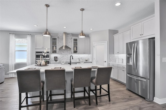 kitchen featuring white cabinets, decorative light fixtures, wall chimney range hood, dark hardwood / wood-style floors, and stainless steel fridge with ice dispenser