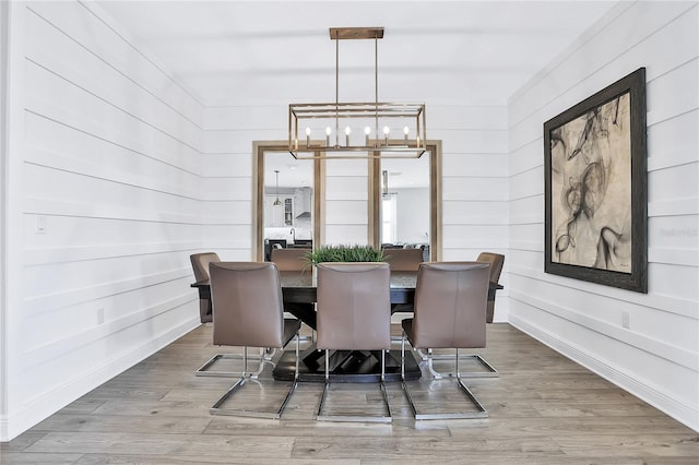 dining room featuring wood walls, light wood-type flooring, and a chandelier