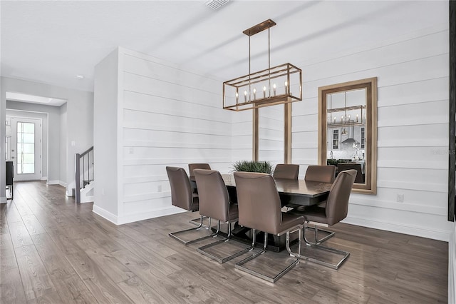 dining area with hardwood / wood-style flooring, wooden walls, and an inviting chandelier