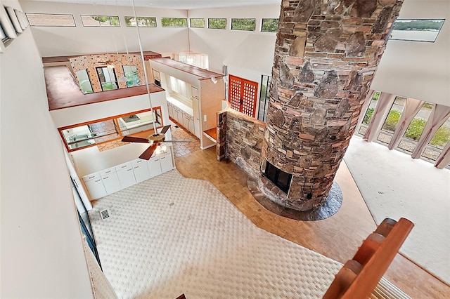 living room with ceiling fan, a stone fireplace, a towering ceiling, and a healthy amount of sunlight