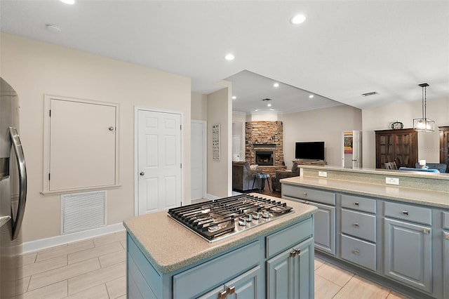 kitchen with appliances with stainless steel finishes, a stone fireplace, pendant lighting, a kitchen island, and ornamental molding