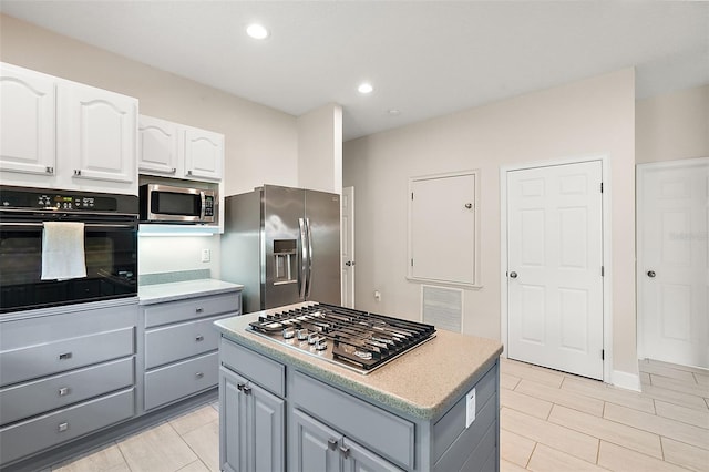 kitchen with appliances with stainless steel finishes, white cabinetry, a kitchen island, and gray cabinetry