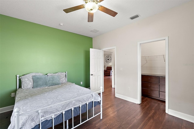 bedroom with a textured ceiling, a walk in closet, a closet, dark wood-type flooring, and ceiling fan