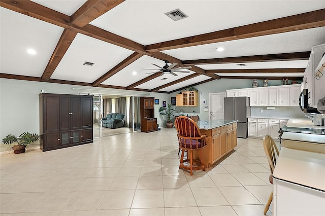 kitchen with a kitchen bar, lofted ceiling with beams, a center island, white cabinets, and stainless steel refrigerator