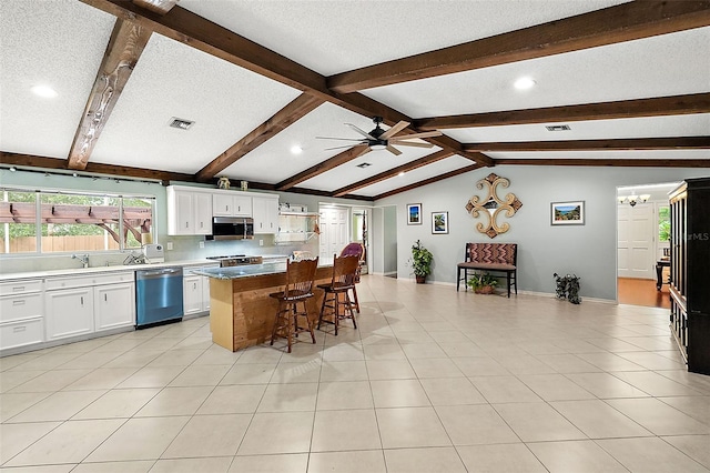 kitchen with appliances with stainless steel finishes, lofted ceiling with beams, a center island, a kitchen breakfast bar, and white cabinets