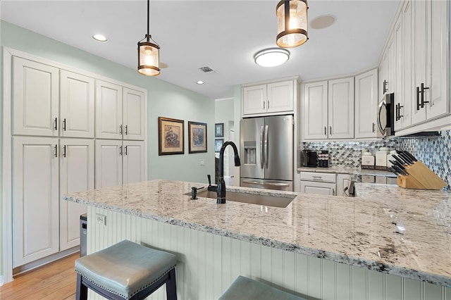 kitchen featuring light wood-type flooring, appliances with stainless steel finishes, pendant lighting, and white cabinetry