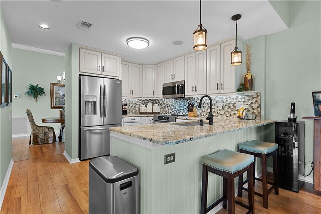 kitchen featuring decorative light fixtures, light hardwood / wood-style floors, stainless steel appliances, kitchen peninsula, and light stone counters