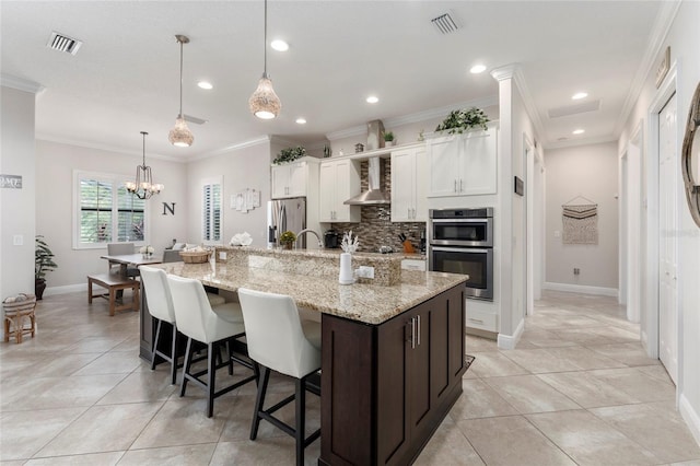 kitchen with appliances with stainless steel finishes, a kitchen island with sink, hanging light fixtures, a breakfast bar, and white cabinets