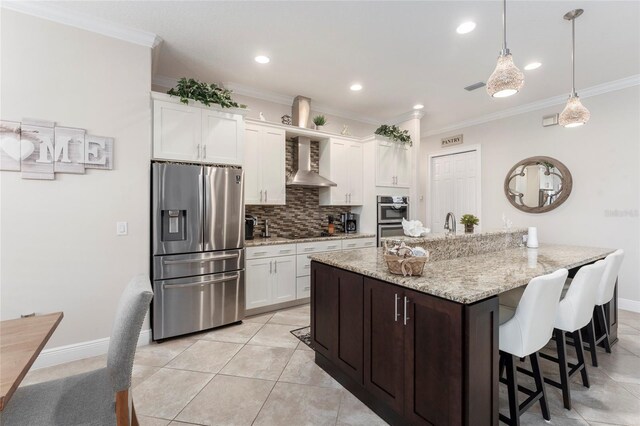 kitchen featuring a center island with sink, pendant lighting, stainless steel appliances, wall chimney range hood, and white cabinets