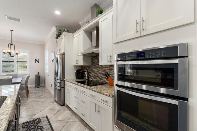 kitchen with white cabinets, an inviting chandelier, appliances with stainless steel finishes, light stone countertops, and wall chimney range hood