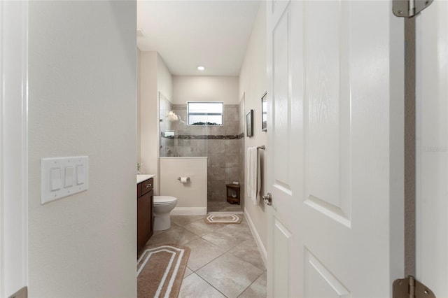 bathroom with tiled shower, tile patterned flooring, toilet, and vanity