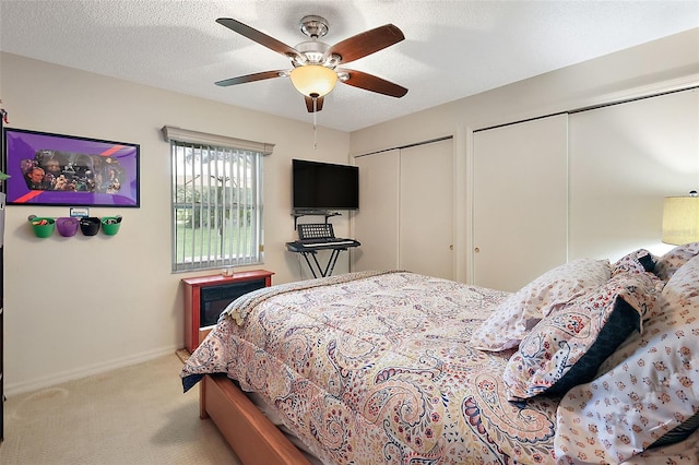 bedroom with carpet floors, a textured ceiling, ceiling fan, and multiple closets