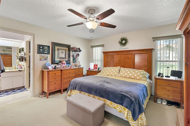 bedroom with a textured ceiling, connected bathroom, light carpet, and ceiling fan